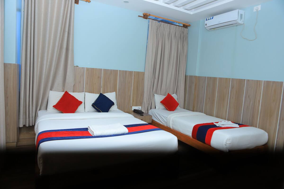 Una habitación de hotel con dos camas, un cabecero de madera, un aire acondicionado y una ventana con cortinas.