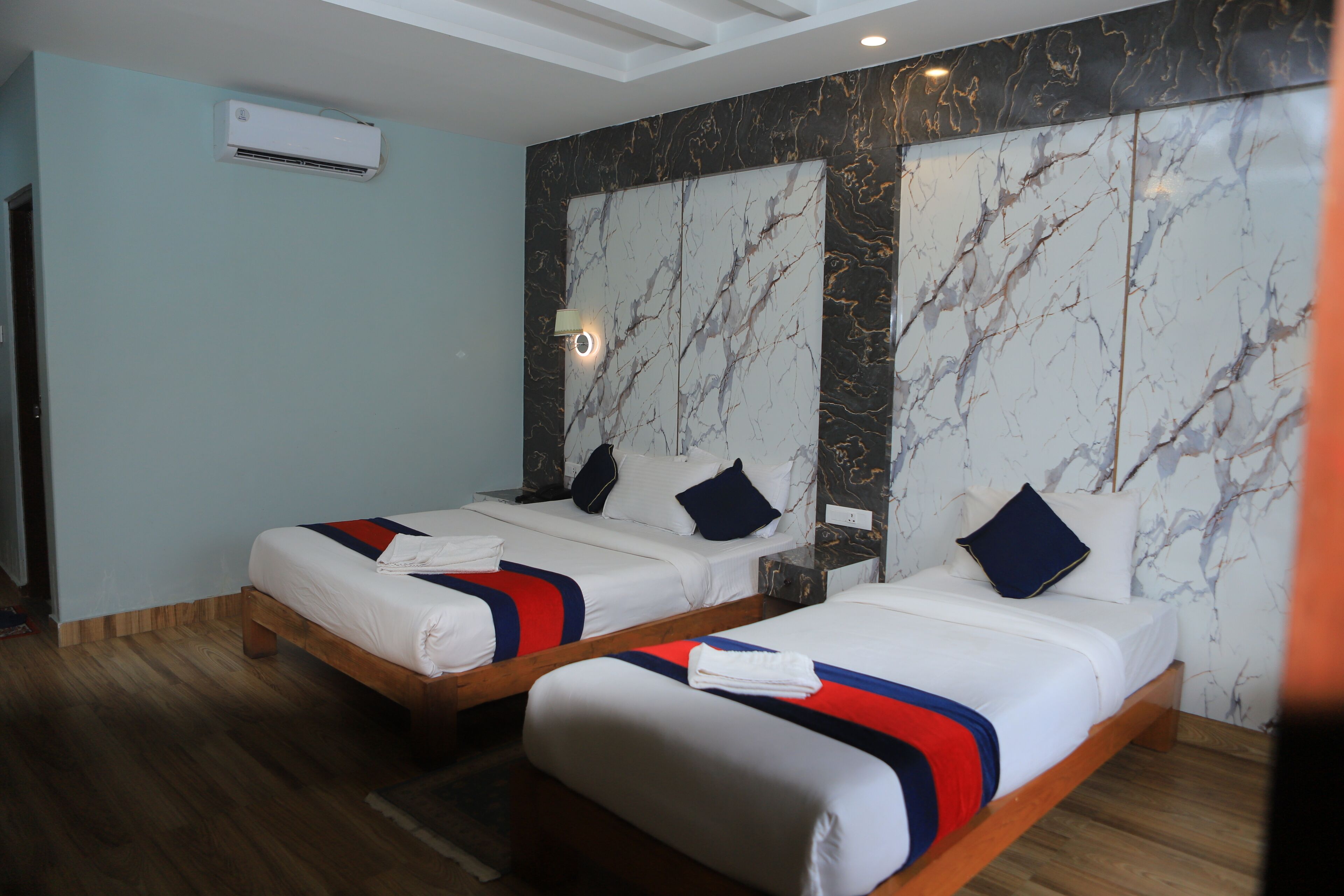 Habitación de hotel con dos camas, paneles de pared de mármol, ventilador de techo y aire acondicionado.