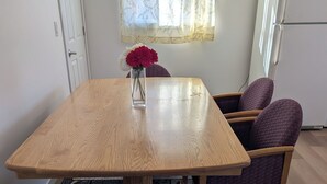 A dining area with a wooden table, four purple chairs, a vase with flowers, and a patterned rug.