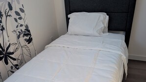 A neatly made bed with a white duvet and pillows, a dark headboard, and a floral-patterned curtain.
