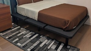 A bed with a headboard, a bedside table, and a patterned rug.