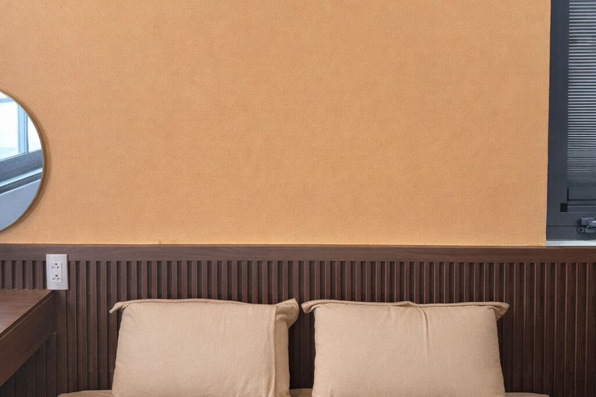 Un dormitorio con pared color beige, cabecero de madera y cama con ropa de cama color beige.