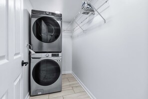 Una sala de lavandería con dos lavadoras apiladas de carga frontal y un tendedero.