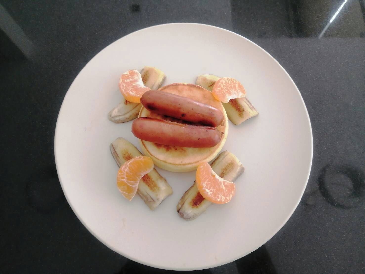 A plate with two sausages, bananas, and orange slices.