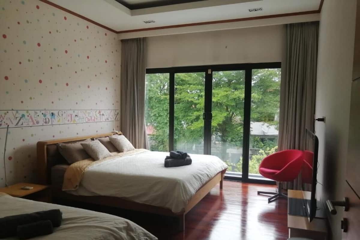 Habitación de hotel con una cama grande, una cama más pequeña, una silla roja, un televisor y una ventana con vistas a árboles.