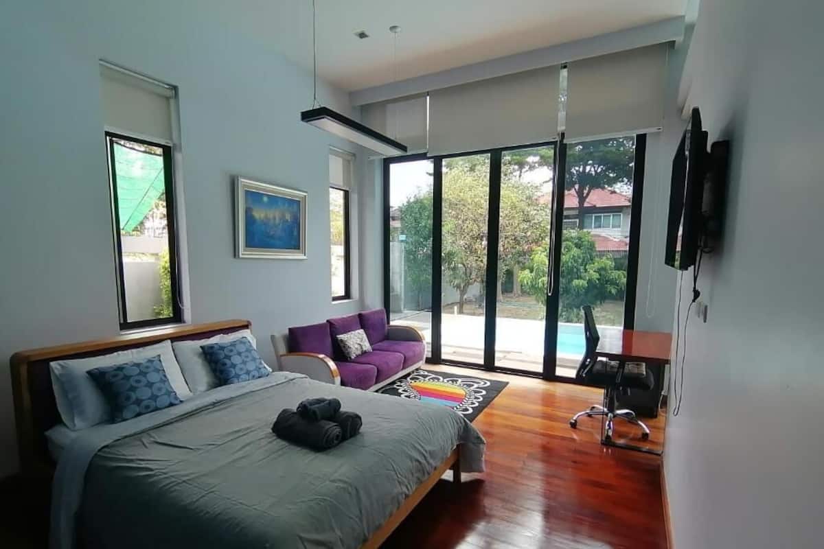 Un dormitorio con una cama, un sofá púrpura, un televisor y un ventanal grande.