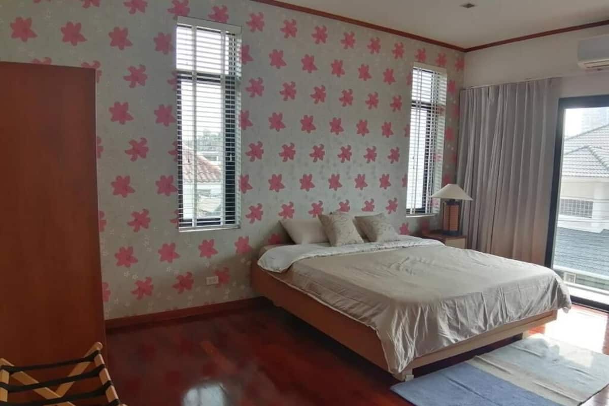 Un dormitorio con una cama, una silla de madera, una mesita de noche y una ventana con cortinas.