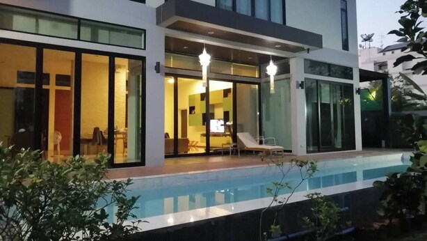 A modern two-story house with a swimming pool, large windows, and a covered patio area.