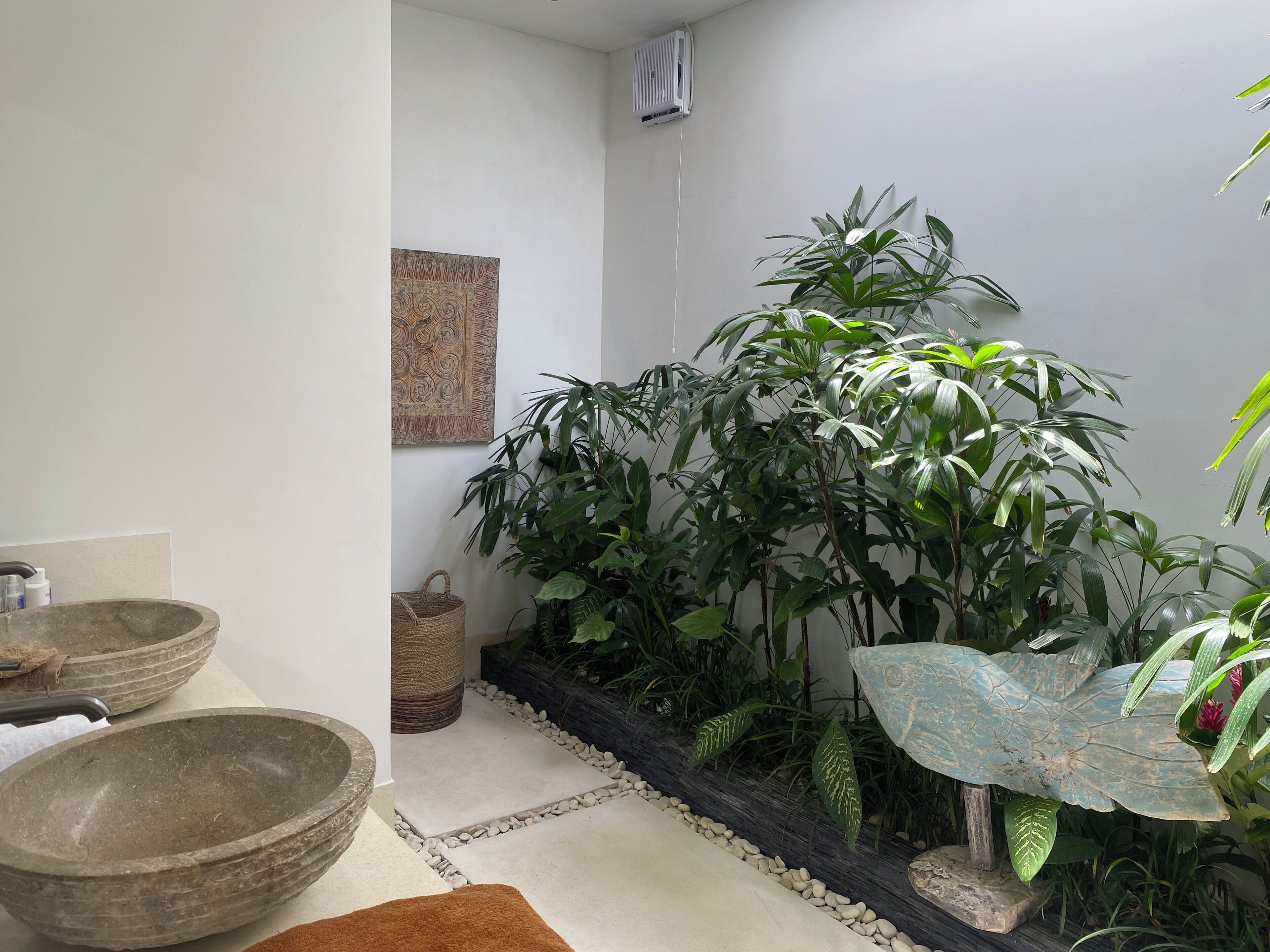 Un baño con un lavabo de piedra, una cesta trenzada y una planta grande en maceta.