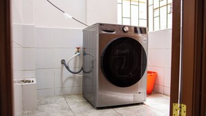 Een kleine, moderne wasruimte met een voorlader wasmachine, een kleine verwarming en een oranje emmer.