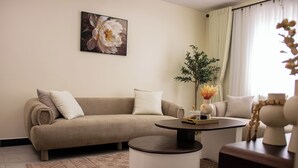Een woonkamer met een beige bank, een ronde salontafel en een groot bloemen schilderij aan de muur.