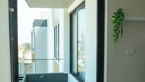 Um corredor moderno com porta de vidro que dá para uma varanda, um vaso de planta e uma escada visível.
