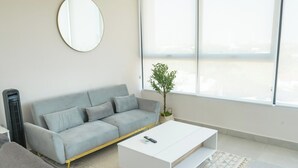 Uma sala de estar moderna com um sofá cinzento, uma mesa de centro branca e uma janela ampla.