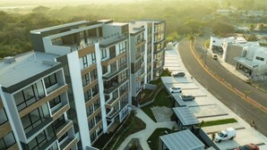 Edifício residencial com várias andares, varandas, área de estacionamento e uma estrada ao fundo.