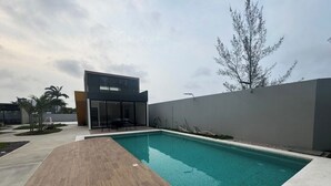 Uma piscina moderna ao ar livre com um deck de madeira, um alpendre envidraçado e uma parede cinzenta.