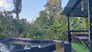 Una piscina circondata da vegetazione rigogliosa, un pontile in legno e un’area salotto coperta.