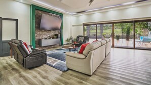 Ein modernes Wohnzimmer mit einer Couch, Relaxsessel, Flachbildfernseher und einer großen Glasschiebetür, die auf eine Terrasse im Freien führt.