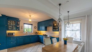 A kitchen with blue cabinets, a wooden dining table, and a window with curtains. - Charming 5-person Villa by the sea (Callantsoog)