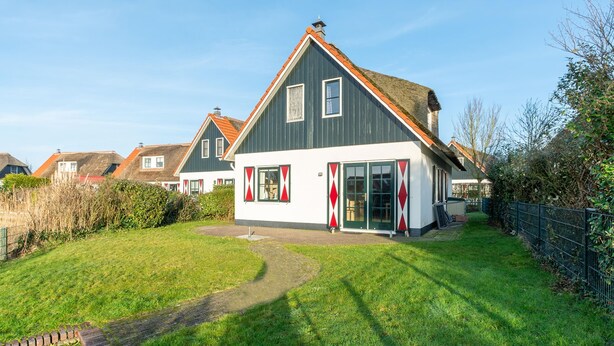 A modern house with a sloped roof, large windows, and a well-maintained lawn. - Charming 5-person Villa by the sea (Callantsoog)