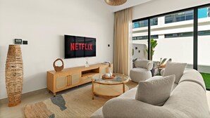 Una sala de estar moderna con un televisor de pantalla plana grande, un mueble bajo de madera, una mesa de centro de vidrio y un sofá color beige.