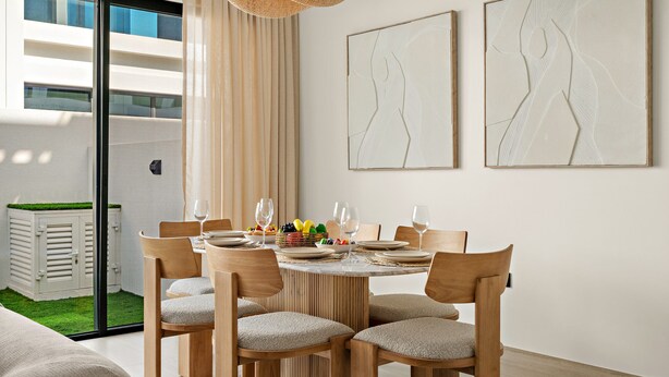 Un comedor con una mesa redonda, sillas de madera y vistas a un jardín por un ventanal corredero.