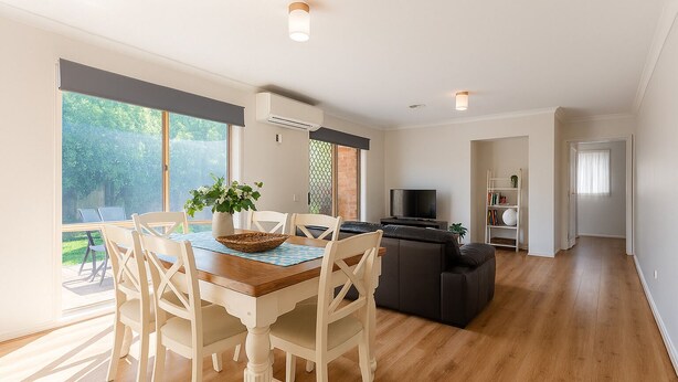 Ein geräumiges Wohnzimmer mit Holzboden, einem Essbereich mit Tisch und Stühlen, einem schwarzen Sofa und einem Fernseher.