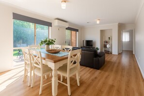 Amplia sala de estar con piso de madera, un comedor con mesa y sillas, un sofá negro y un televisor.