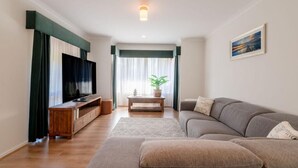 Ein modernes Wohnzimmer mit einer Couch, einem Hocker, einer Holz-Unterhaltungseinrichtung und einem Fernseher.