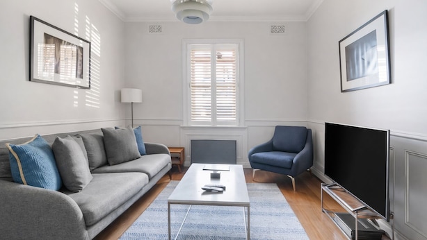 A modern living room with a grey sofa, a blue armchair, a coffee table, and a flat-screen TV. - Luxury Spacious 3BR Family Home Walk To Harbour Bridge/ Opera House& CBD (Millers Point)