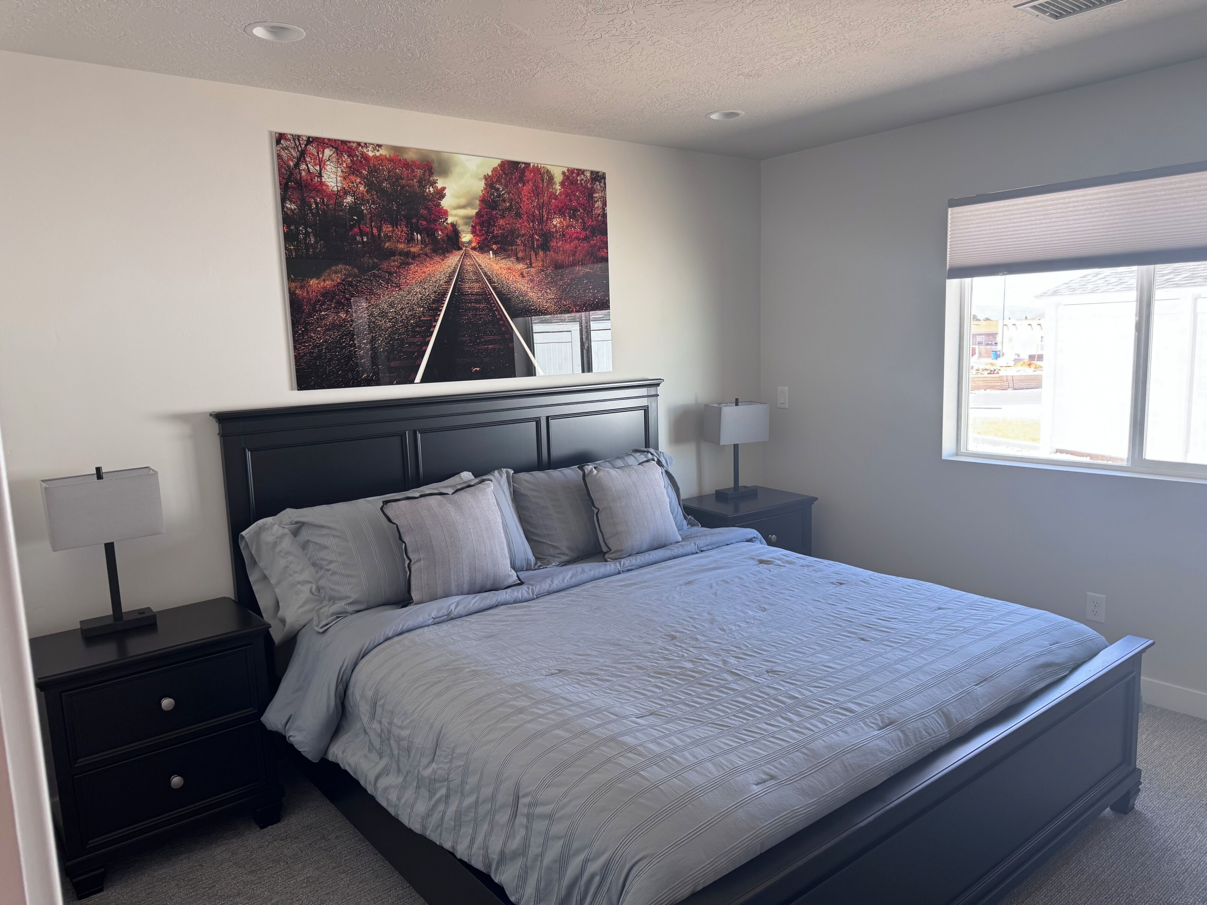A bedroom with a bed, nightstands, a window, and a painting on the wall.