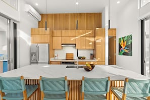 A modern kitchen with wooden cabinets, a large island, and a dining area with woven chairs.