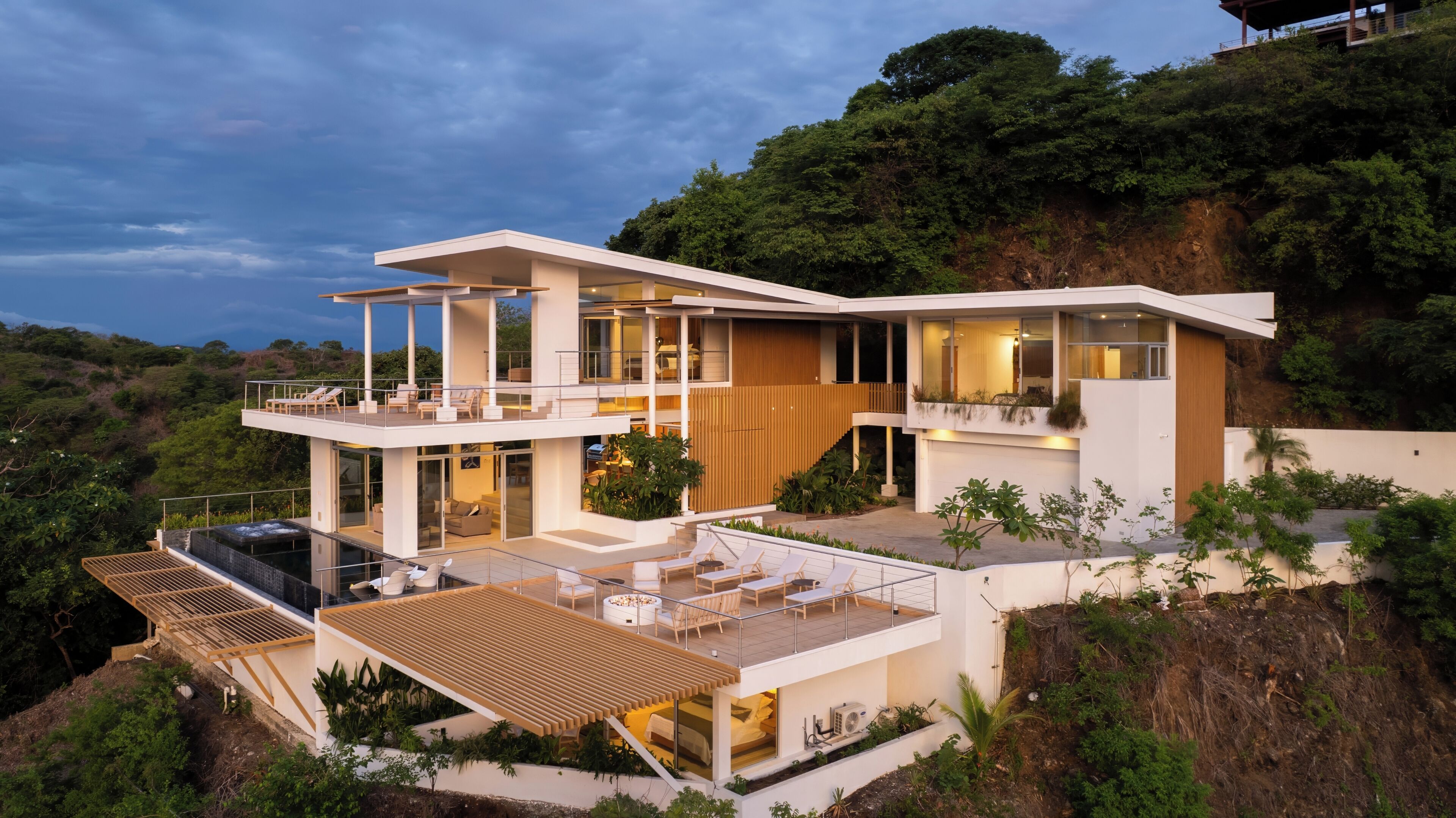 A modern two-story house with a pool, outdoor seating, and a view of the surrounding landscape.