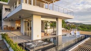 A modern house with a large glass balcony, a swimming pool, and a view of the surrounding landscape.