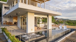 A modern house with a large glass balcony, a swimming pool, and a view of the surrounding landscape.