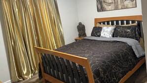 Ein Schlafzimmer mit Bett, Holz-Kopfteil, Nachttisch, Buddha-Statue und einem Gemälde an der Wand.
