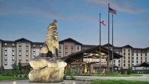 Ein Hotel mit einer großen Felsformation im Vordergrund, einem Schild mit der Aufschrift "Great Wolf Lodge" und zwei Wimpeln auf Fahnenmasten.