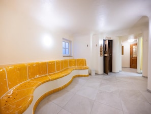 Um corredor com um banco amarelo, uma janela e uma porta que dá para outro quarto.