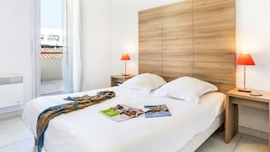 A hotel room with a large bed, two bedside tables, a wooden headboard, and a view through a sliding door. - Cap Med by Interhome (Le Grau du Roi)