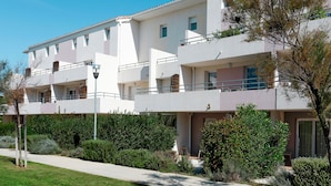 A multi-story hotel with balconies, a paved walkway, and well-maintained landscaping. - Cap Med by Interhome (Le Grau du Roi)