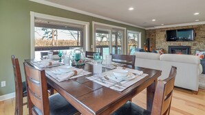 Un coin repas avec une table en bois dressée pour quatre personnes, une cheminée en pierre et un téléviseur fixé au mur.