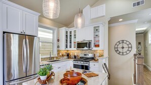 A modern kitchen with white cabinets, stainless steel appliances, and a central island with a wooden bowl and cutting board. - Walk to Bay & Pleasure Pier! Catalina Island Stay (Avalon)