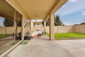 Un patio couvert avec un sol en béton, un ventilateur de plafond et une vue sur le jardin arrière.