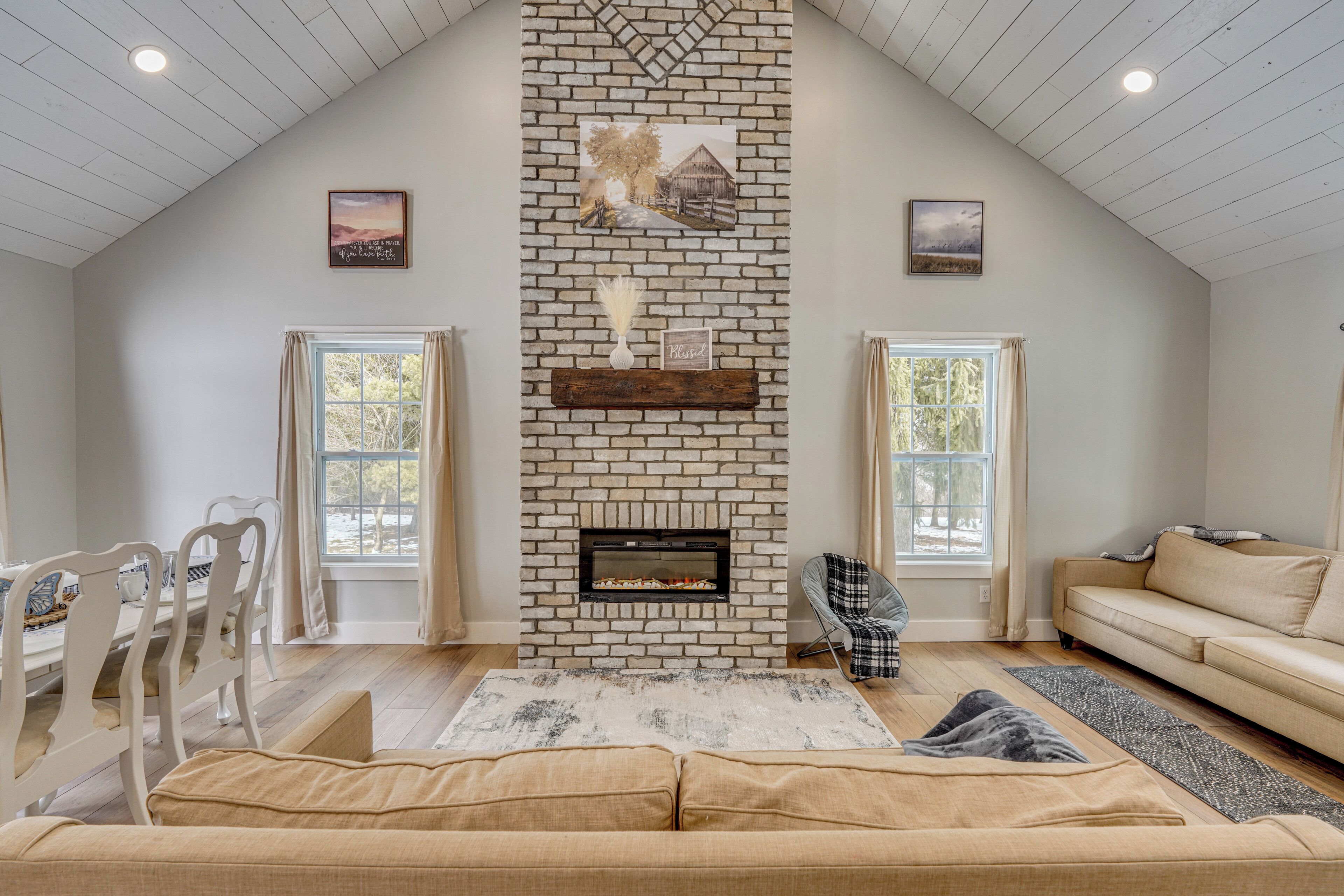 A spacious living room with a high ceiling, a fireplace, a dining area with chairs, and a sofa.