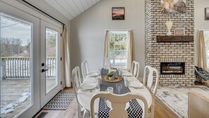 A dining area with a brick fireplace, large windows, and a view of the outdoors.