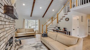 A spacious living room with a fireplace, two sofas, a staircase, and a dining area.