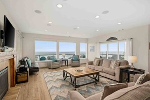 A spacious living room with a large window overlooking the ocean, a fireplace, and a television mounted on the wall. - Trail’s End: Ocean Views, Hot Tub, Game Room & Beach Access, Pet Friendly, 2 Miles to Casino (Lincoln City)