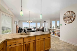 A spacious kitchen with wooden cabinets, pendant lights, a large clock, and a view to the outside. - Trail’s End: Ocean Views, Hot Tub, Game Room & Beach Access, Pet Friendly, 2 Miles to Casino (Lincoln City)