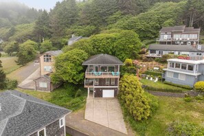 Une maison à deux étages dotée d’un balcon, entourée d’une végétation luxuriante et d’autres immeubles résidentiels.