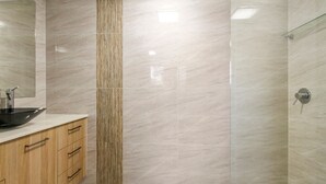 Baño con un lavamanos negro tipo recipiente, armarios de madera y un columnilla texturizada vertical.