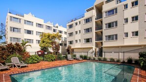 Un edificio residencial con piscina, varios balcones y un sendero de ladrillos.
